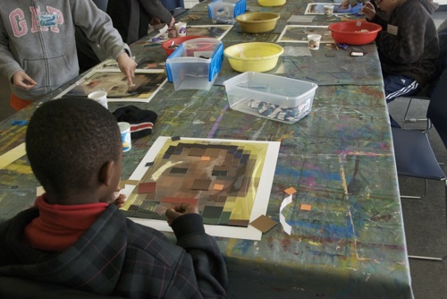 Students glue squares of color on paper to represent faces